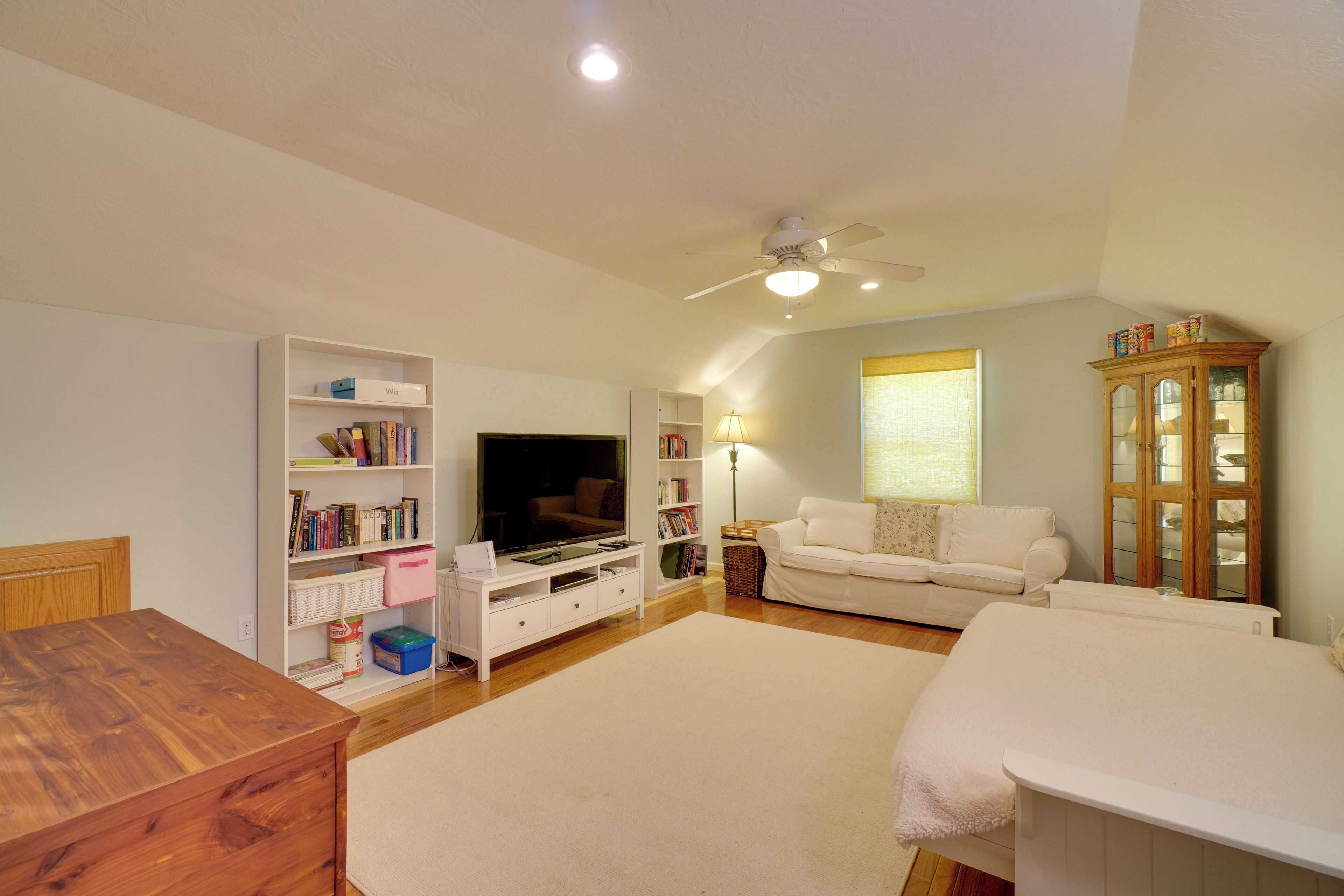Una sala de estar con televisor, sofá blanco, mueble de madera y ventilador de techo.