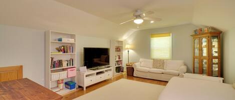 Una sala de estar con televisor, sofá blanco, mueble de madera y ventilador de techo.