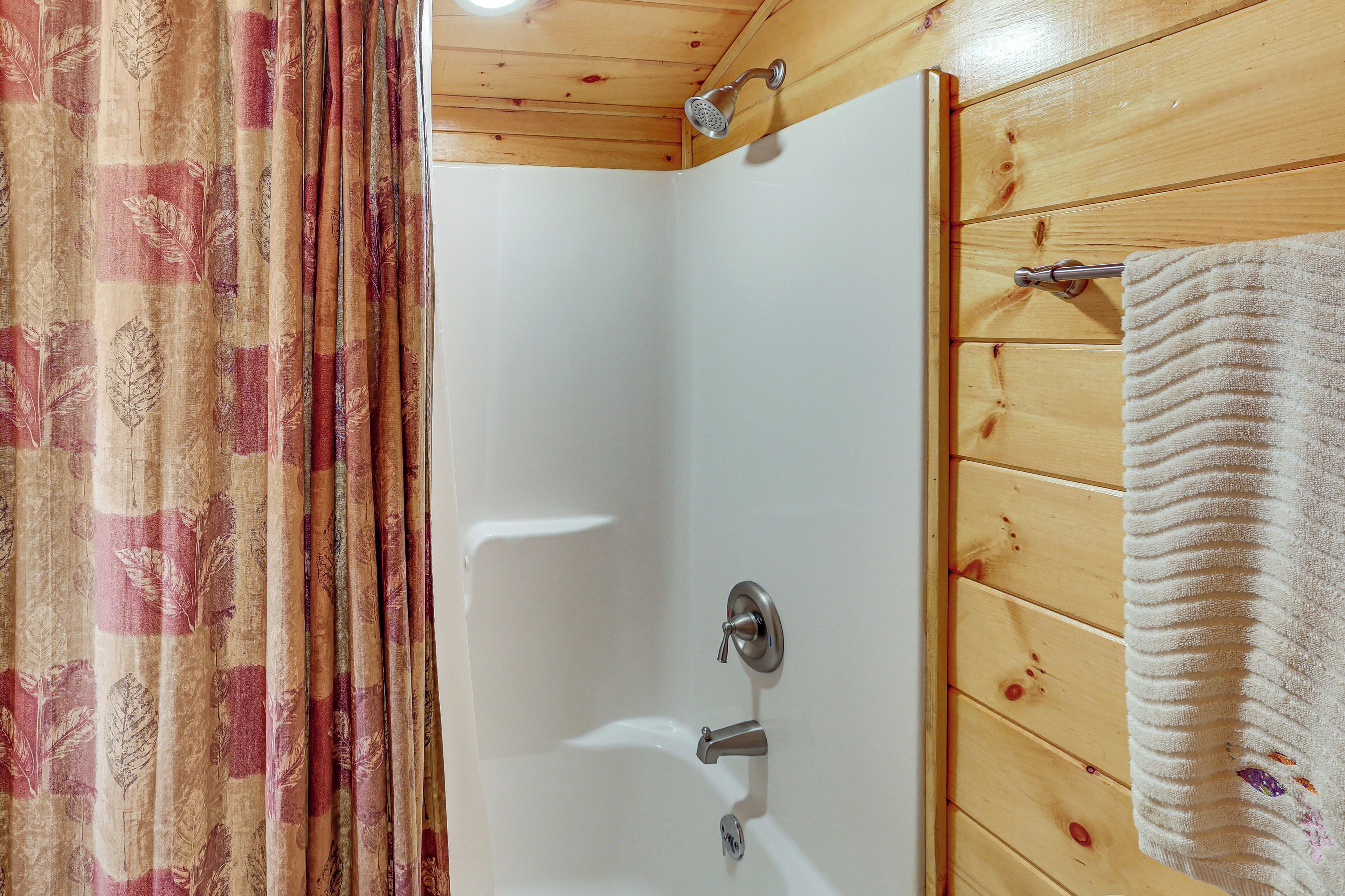 A shower with a wooden wall, a towel hanging on the wall, and a curtain with a leaf pattern.