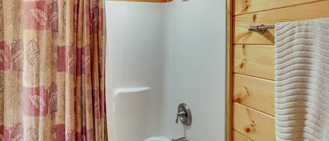 A shower with a wooden wall, a towel hanging on the wall, and a curtain with a leaf pattern.