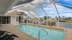 An indoor swimming pool with a covered area, lounge chairs, and a view of the water body outside. - Waterfront Pool Home by Park Pickleball Sleeps 10 (Cape Coral)