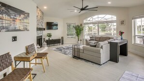A spacious living room with a fireplace, a ceiling fan, and large windows. - Waterfront Pool Home by Park Pickleball Sleeps 10 (Cape Coral)