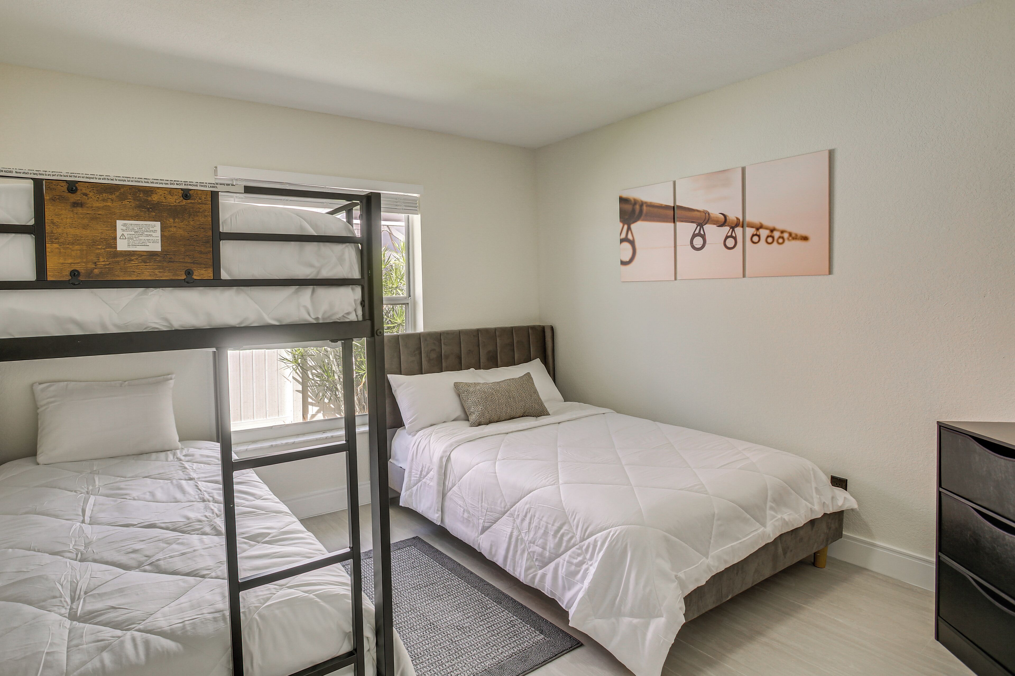 Een kamer met een stapelbed, een eenpersoonsbed, een houten hoofdeinde, een grijze vloerkleed en een wanddecoratie.