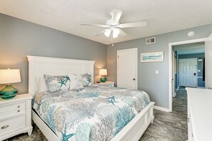 Ein Schlafzimmer mit Bett, Nachttischen, Deckenventilator, Tür und einem Flur.