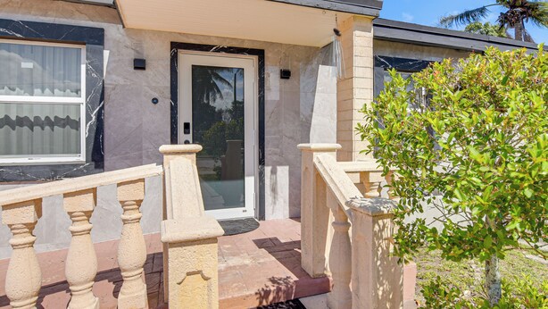 A building with a glass door, a stone staircase, and a small tree in the foreground. - 4 Mi to Hard Rock Stadium & Lakes! Elegant Home (Opa-locka)