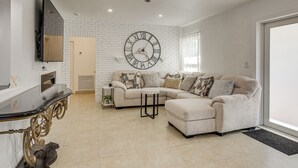 A living room with a sectional sofa, a round wall clock, a flat-screen TV, and a fireplace. - 4 Mi to Hard Rock Stadium & Lakes! Elegant Home (Opa-locka)