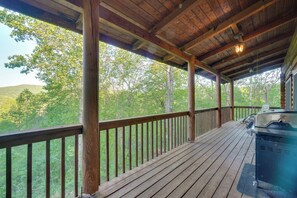 Eine überdachte Terrasse im Freien mit Grill, Holzgeländern und Blick auf ein bewaldetes Gebiet.