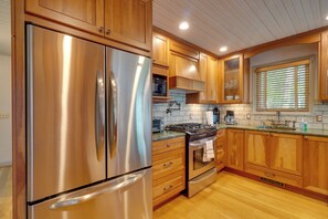 Una cocina con armarios de madera, electrodomésticos de acero inoxidable y un ventanal con persianas.
