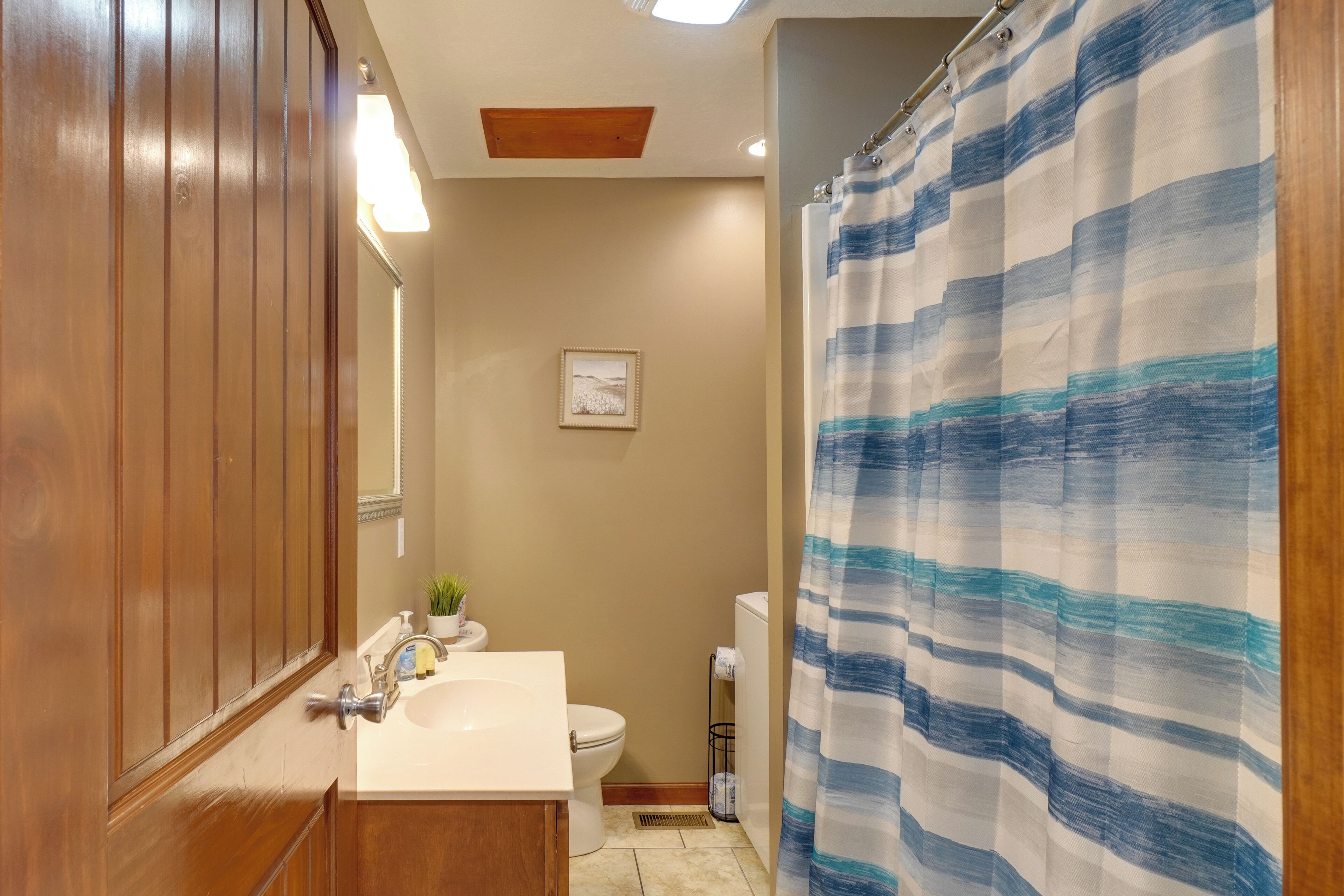 Une salle de bain avec un meuble-lavabo en bois, un lavabo blanc, des toilettes et un rideau de douche à motifs bleus et blancs.