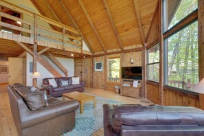 Ein geräumiger Wohnbereich mit hoher Decke, Holzbalken, Ledersofas, einem Couchtisch und einem Fernseher.