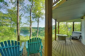 Een houten terras met Adirondack-stoelen met uitzicht op een meer, omgeven door bomen.
