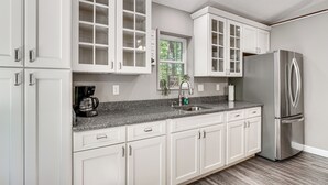 A modern kitchen with white cabinetry, a stainless steel refrigerator, and a granite countertop. - 2 Mi to Dale Hollow Lake! 'Shadowood' Group Escape (Byrdstown)