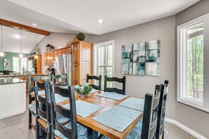 Un comedor con mesa de madera, sillas y cocina al fondo.