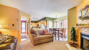 A living room with a sofa, a fireplace, and a dining area with chairs and a table. - Walk to Angel Fire Resort! Mtn-View Condo Near Fun (Angel Fire)