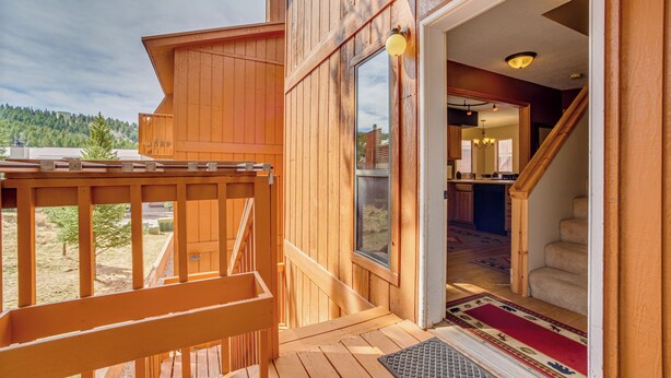 A wooden deck with a bench, a door leading to a staircase, and a view of a forested area. - Walk to Angel Fire Resort! Mtn-View Condo Near Fun (Angel Fire)