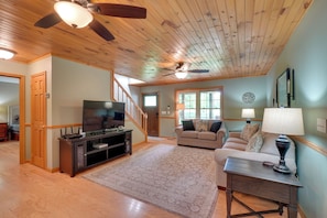 A spacious living room with a wooden ceiling, a television, a sofa, a coffee table, and a staircase leading to another room.
