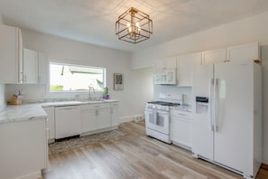 A modern kitchen with white cabinetry, a built-in oven, microwave, and refrigerator, a wooden floor, and a geometric pendant light. - Fire Pit & Amazing Views! 15-Acre Colfax Farmhouse (Colfax)