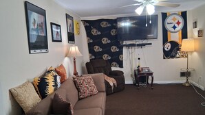 A living room with a brown sofa, a ceiling fan, a TV, and a Steelers-themed wall. - Peaceful 1-bedroom rental in home 20 mins from Downtown! (Decatur)