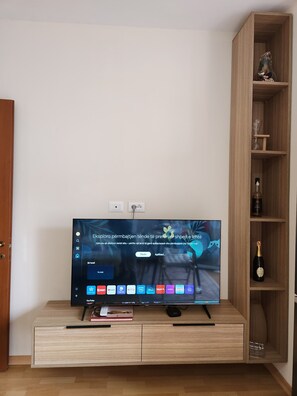 Un téléviseur à écran plat posé sur un meuble télé en bois, avec une télécommande, un livre et une souris d’ordinateur à proximité.