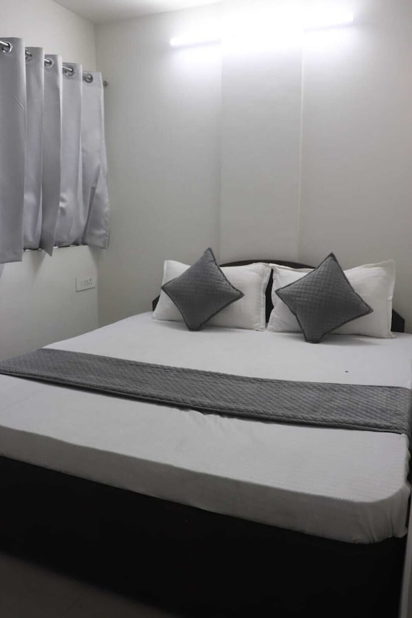 A bed with a white mattress, grey pillows, and a grey blanket.