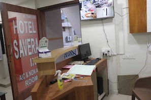 A hotel reception desk with a computer, a phone, and a sign indicating A&C & NON A rooms. - Hotel Savera Inn (Ahmedabad)