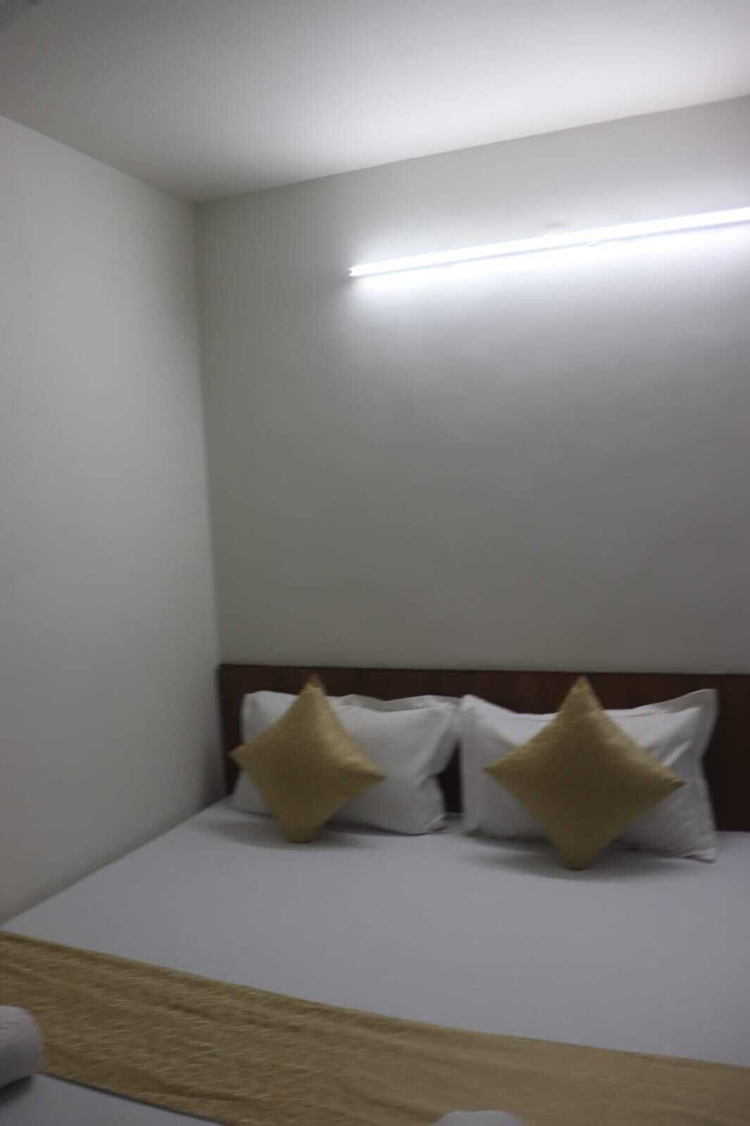 A hotel room with a single bed, white bedding, and two gold pillows.