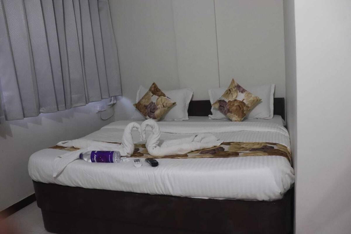A hotel room with a bed, pillows, a water bottle, and a remote control.