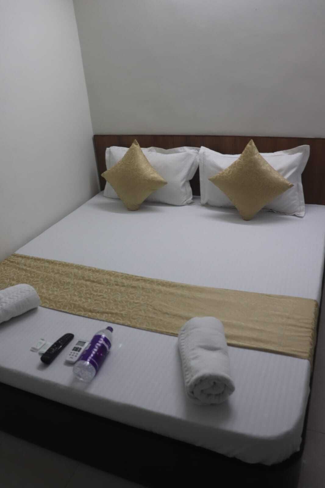 Una habitación de hotel con una cama, dos almohadas, una manta, una toalla enrollada y un control remoto.