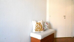 Um quarto com uma porta branca, um banco com almofada branca e duas almofadas com texto.