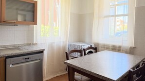 Uma cozinha equipada com máquina de lavar louça, mesa, cadeiras, máquina de lavar roupa e uma janela com cortinas.