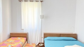 Quarto com duas camas, mesa de cabeceira, abajur e janela com cortinas.