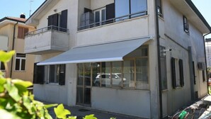 Um edifício residencial de dois andares com varanda, janelas amplas e toldo branco.