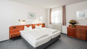 Een tweepersoonsbed met houten hoofdeinde, een nachtkastje, een dressoir en een raam met gordijnen.
