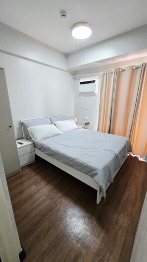 Ein Schlafzimmer mit Bett, Nachttisch, Klimaanlage und Vorhängen.