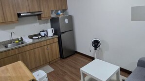 Ett kompakt kök med träskåp, ett kylskåp, en spis och en diskho. Där finns ett matbord med stolar, ett vitt soffbord och en grå soffa.