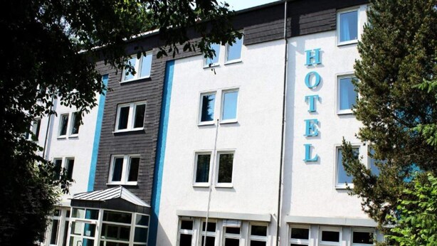 Un edificio de hotel con un llamativo letrero 'HOTEL', amplias ventanas y un área de entrada cubierta.