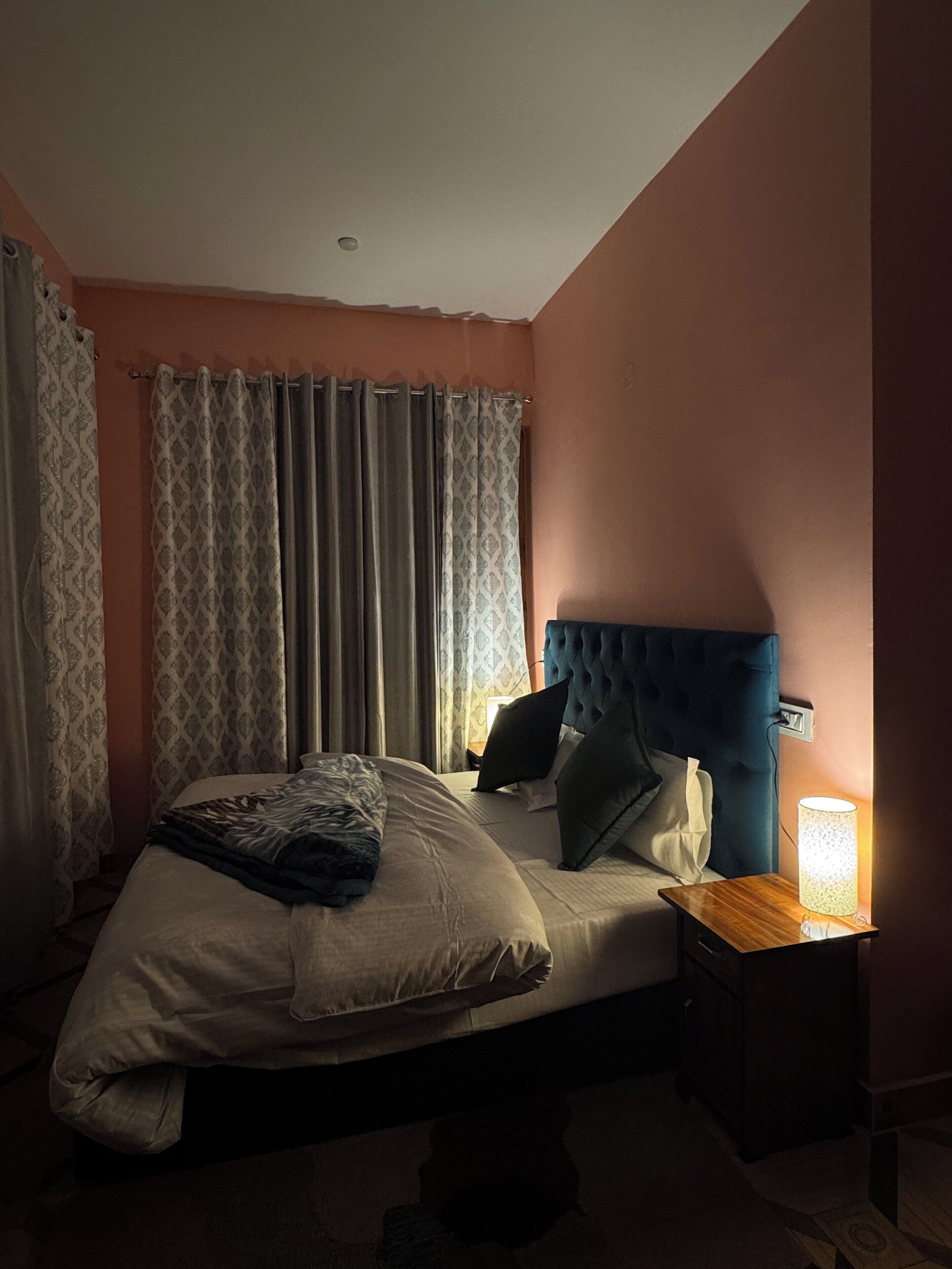 A bedroom with a bed, curtains, a nightstand, and a lamp.