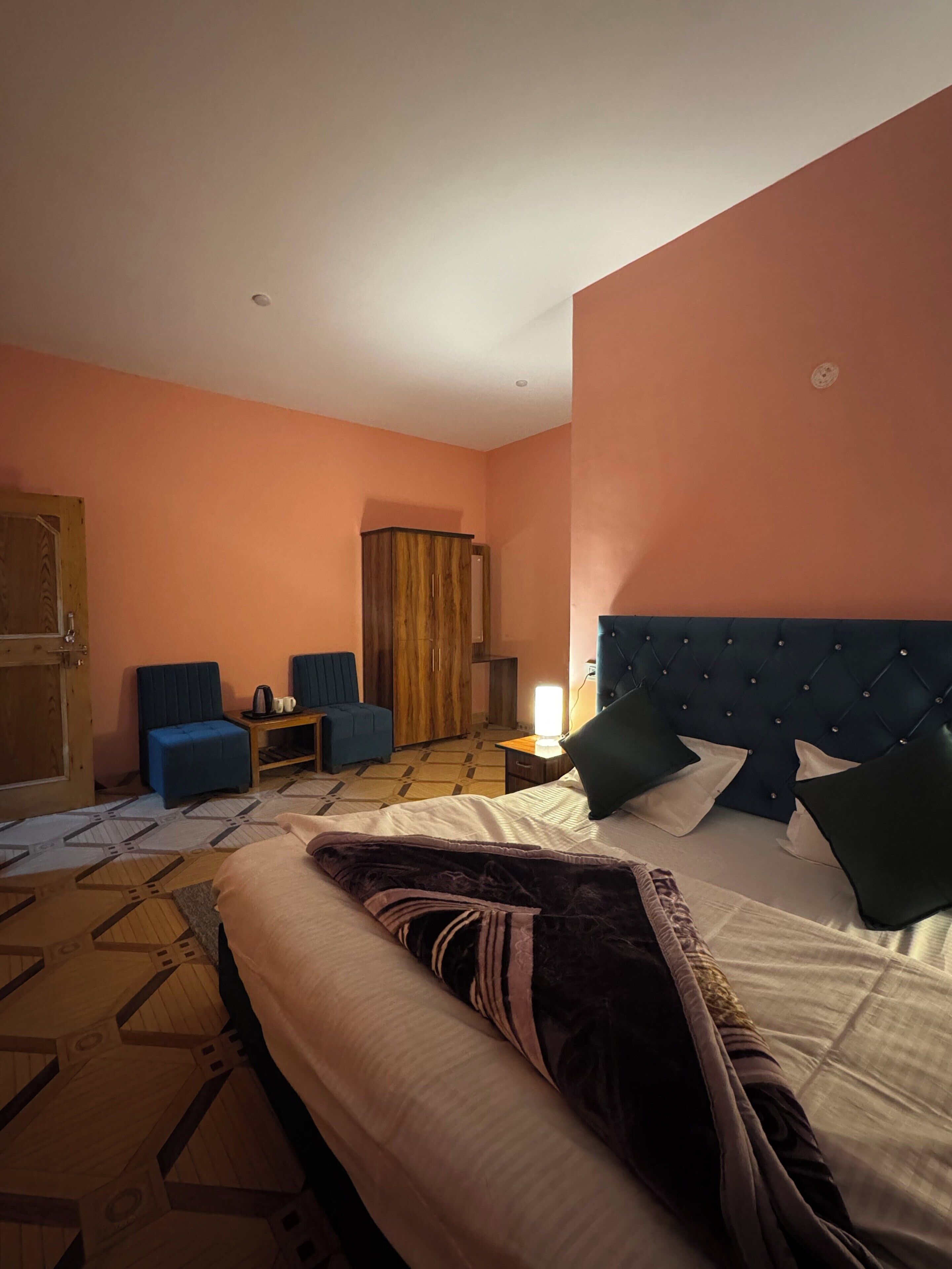 A hotel room with a bed, a wardrobe, a desk, a chair, and a lamp.