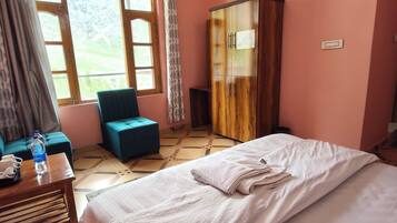 Una habitación de hotel con cama, un sillón azul, un armario de madera y una ventana con cortinas.
