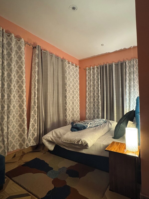Een slaapkamer met een bed, gordijnen, een nachtkastje en een lamp.
