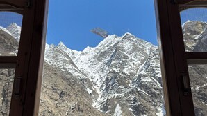 Blick durch ein Holzfenster auf schneebedeckte Berge unter blauem Himmel.
