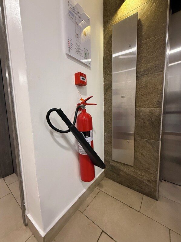 Un extintor colgado en una pared, una caja roja de emergencia y una puerta de ascensor metálica.