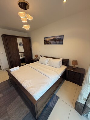 Une chambre à coucher avec un grand lit, une table de chevet, une lampe, une armoire et un tableau représentant un paysage urbain accroché au mur.