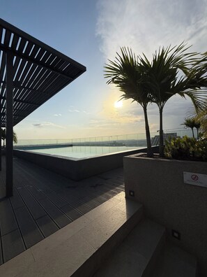 Una piscina en la azotea con vista al horizonte de la ciudad, un cartel de no fumar y una palmera.