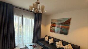 Een moderne woonkamer met een zwarte leren bank, een glazen salontafel en een kroonluchter.