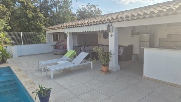Un espace extérieur abrité comprenant des chaises longues, une piscine et une terrasse avec une table et des chaises.