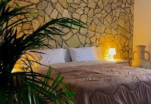 A bed with a stone wall backdrop, a bedside lamp, and a potted plant. - Apartment Sleeps 6 With Parking (Trapani)