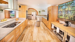 Una cocina moderna con armarios de madera, una isla central y un amplio ventanal con vistas a palmeras.