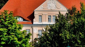 A building with a red-tiled roof, a central decorative element, and a symmetrical facade. - 4 Person Holiday Park Home in Sagad (Sagard)