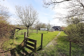 Een landelijk landschap met een grasveld, een houten bankje, een omheind gebied en een gebouw op de achtergrond.